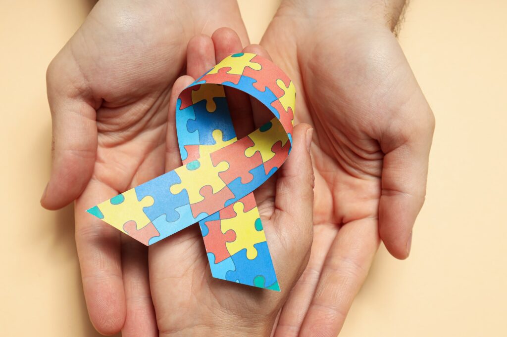 Ribbon with colorful puzzle pieces in hands on light background. World autism day concept